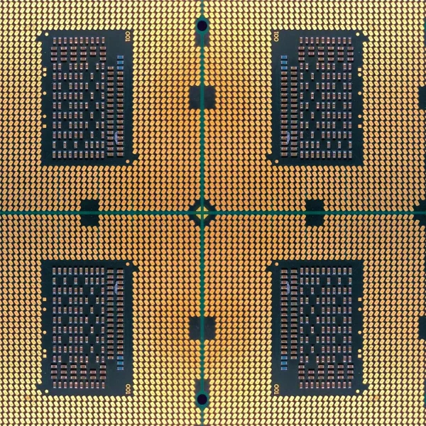 Close-up image of a computer microprocessor, featuring a grid of gold-colored pins on its surface. The geometric pattern reveals four sections with intricate circuit designs, visible through dark rectangles, arranged symmetrically on the chip.