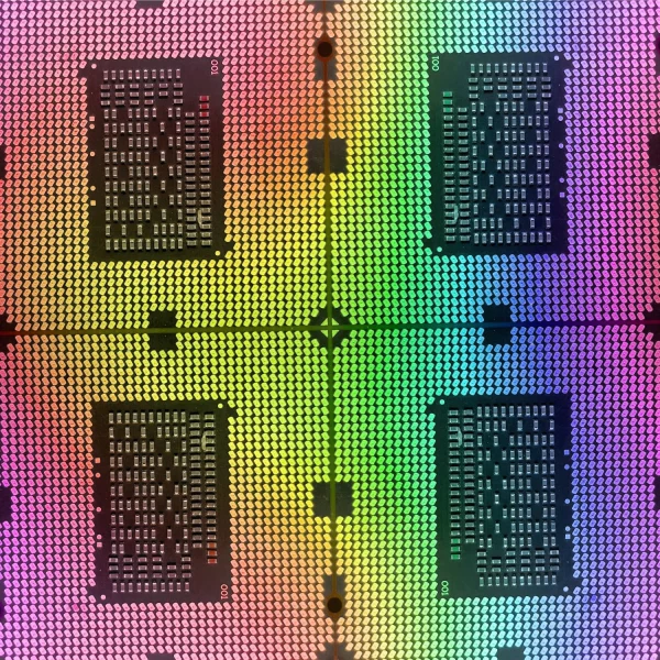 A close-up of a colorful microchip pattern, featuring symmetrical rows of metallic elements on a rainbow-hued background. The design showcases intricate circuitry details bordered by vibrant gradients.