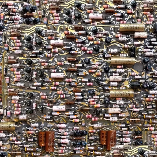 Close-up view of a complex circuit board, featuring numerous electronic components including resistors, capacitors, and diodes arranged in a dense and intricate pattern. The components are various shapes and colors, connected by a network of metal traces.
